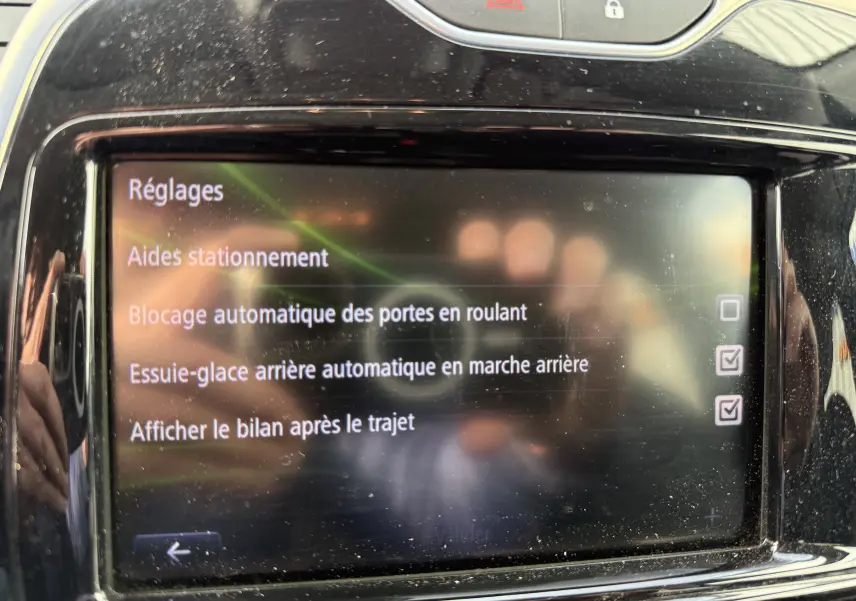 Écran tactile du tableau de bord du Renault Captur blanc 2017 montrant les réglages d’aides au stationnement et verrouillage automatique.