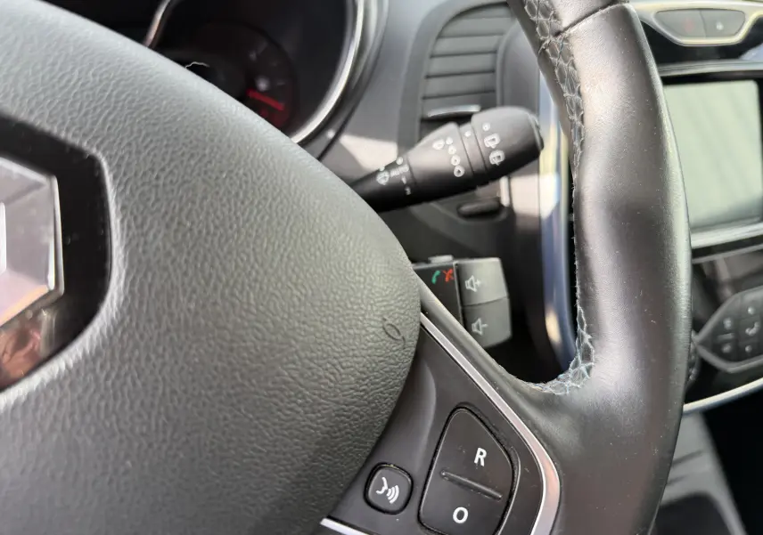 Gros plan sur le volant en cuir noir du Renault Captur blanc 2017, avec commandes intégrées et tableau de bord partiellement visible.