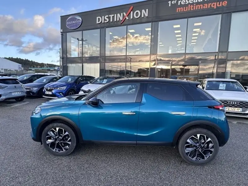 Vue de profil côté gauche d'un DS3 1.2 Hybride 145 Étoile bleu métal avec toit noir, roues au design distinctif, devant un showroom.