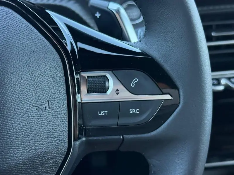 Gros plan sur les commandes gauche du volant du Peugeot 2008 bleu, avec boutons de téléphone et molette de réglage.