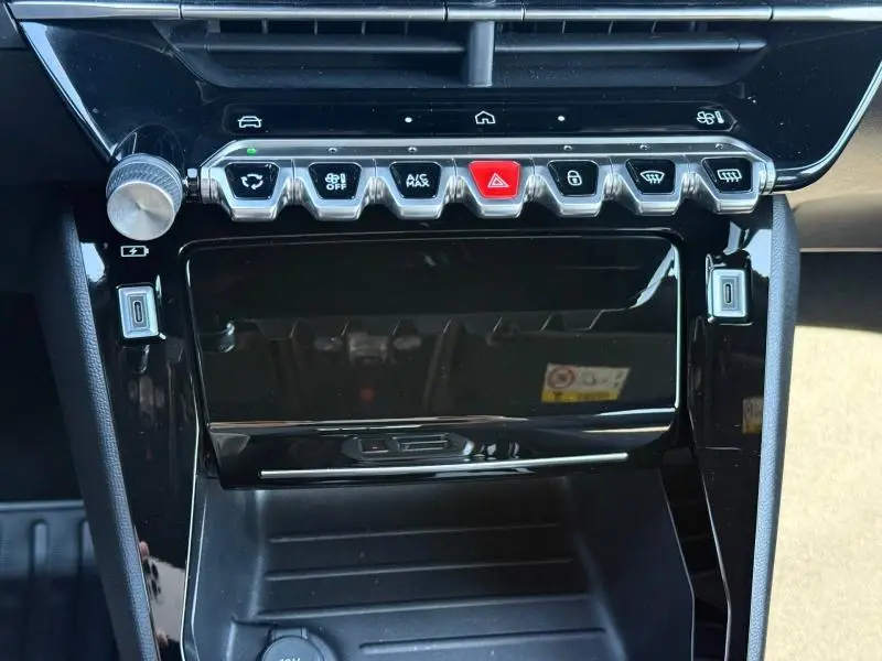 Gros plan sur la console centrale noire brillante du Peugeot 2008 1.2 Hybrid 145ch Allure, avec boutons de commande et finition moderne.