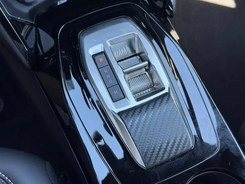 Vue rapprochée de la console centrale noire brillante du Peugeot 2008 Hybrid avec sélecteur de boîte automatique et finition carbone.