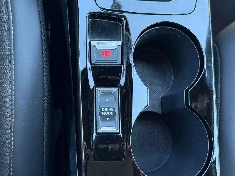 Gros plan sur la console centrale noire brillante du Peugeot 2008 Hybrid 2025, avec bouton Drive Mode et frein à main électronique.