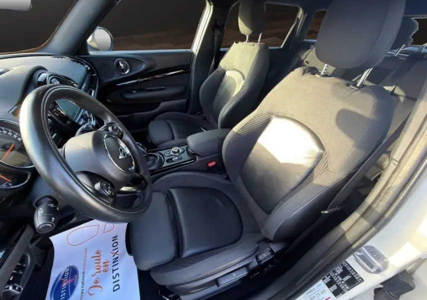 Intérieur avant droit d’une MINI Clubman blanc, sièges en cuir noir et tableau de bord avec écran tactile.