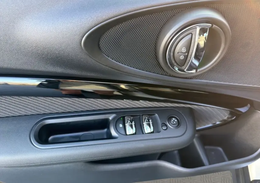Gros plan sur la porte côté conducteur de la MINI Clubman blanche, montrant les commandes de vitres et la poignée intérieure ronde.
