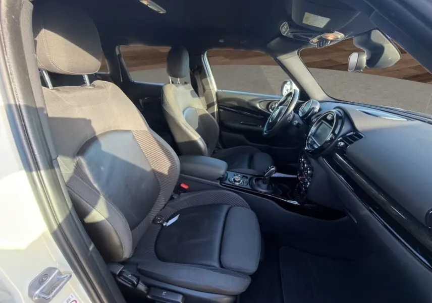 Vue intérieure côté conducteur de la MINI Clubman blanche, montrant sièges noirs et tableau de bord moderne avec écran tactile.