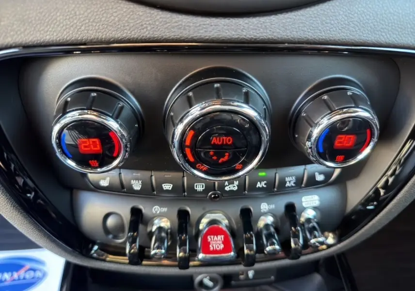 Gros plan sur la console centrale noire de la MINI Clubman blanche, avec commandes de climatisation et bouton rouge Start/Stop.