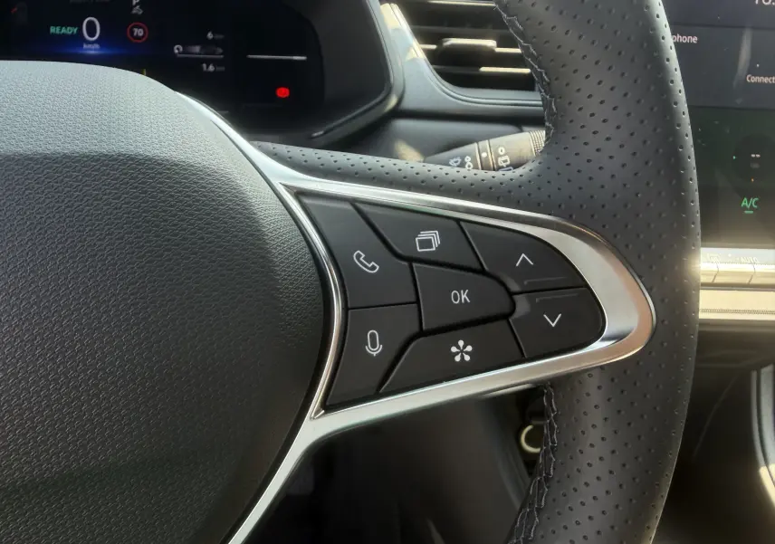 Gros plan sur les commandes multifonctions à droite du volant perforé noir du Renault Captur gris Cassiopée, tableau de bord numérique en arrière-plan.