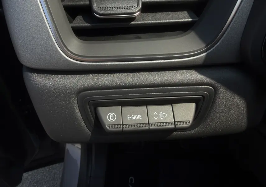 Gros plan sur les commandes sous la grille d’aération intérieure du Renault Captur gris Cassiopée, boutons E-SAVE et réglage des phares.