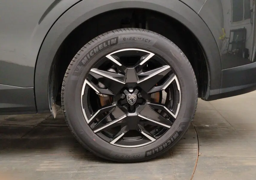 Gros plan sur la roue avant droite du Peugeot 5008 gris titane, jante noire à design géométrique brillant.