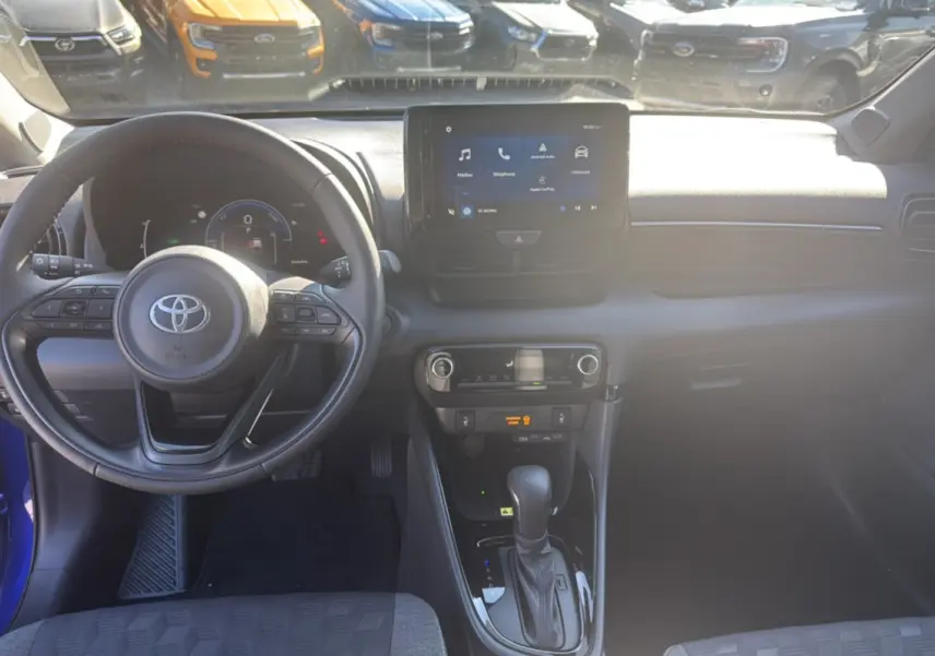 Intérieur de la Toyota Yaris 1.5 Hybrid 2025, vue du poste de conduite avec volant multifonction et écran tactile central.
