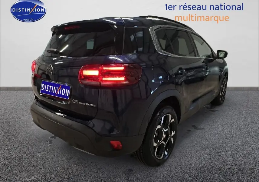 Vue 3/4 arrière droite d'un Citroën C5 Aircross bleu eclipse avec feux arrière allumés en intérieur showroom.