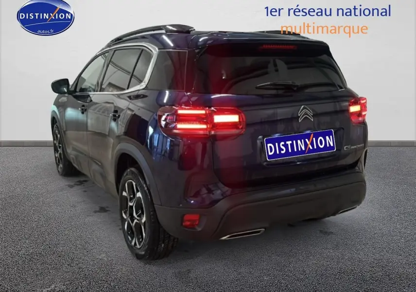 Vue 3/4 arrière droite du Citroën C5 Aircross bleu eclipse avec feux arrière allumés et barres de toit visibles.