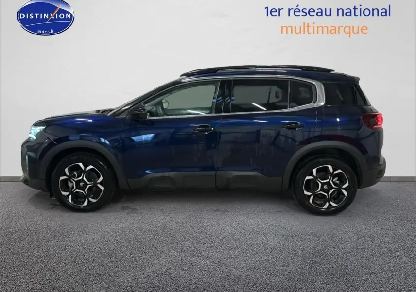 Vue de profil côté gauche d'un Citroën C5 Aircross bleu eclipse avec jantes alliage et barres de toit noires.