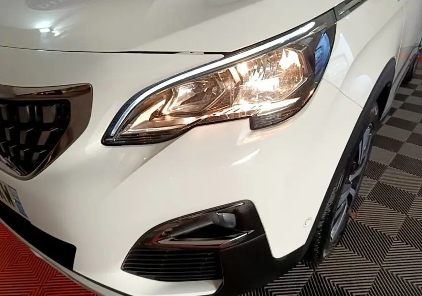 Gros plan sur l'avant droit blanc du Peugeot 3008 hybride, mettant en valeur le phare allumé et la calandre noire.