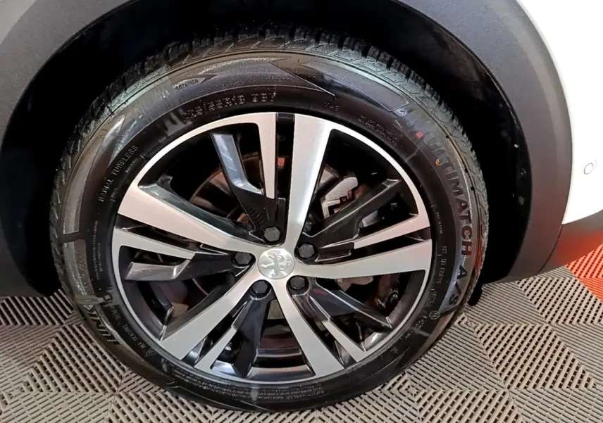 Gros plan sur la roue avant droite du Peugeot 3008 blanc, mettant en valeur la jante alliage bicolore au design moderne.