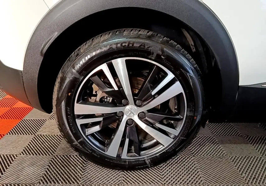 Gros plan sur la roue avant gauche du Peugeot 3008 blanc, mettant en valeur la jante alliage bicolore et le pneu.