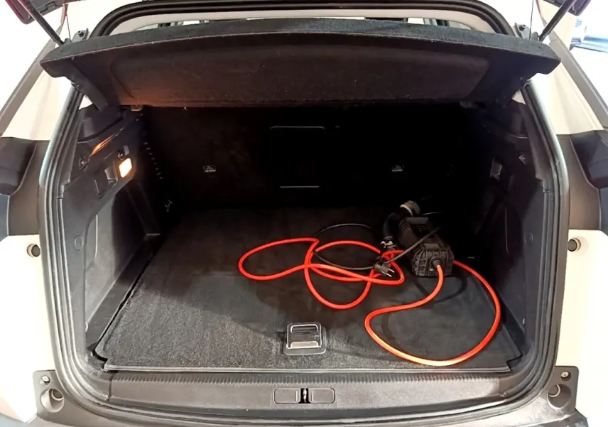Coffre ouvert vu de l'arrière d'un Peugeot 3008 blanc avec câble de recharge hybride visible à l'intérieur.