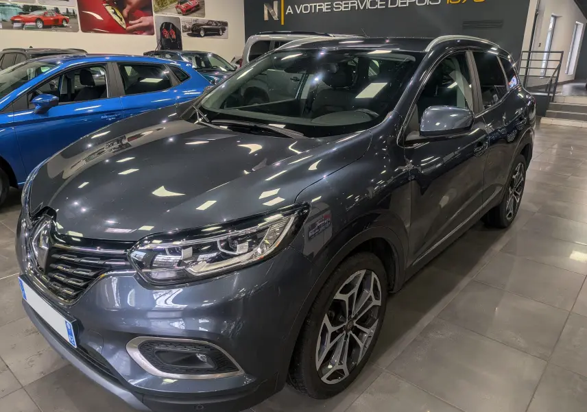 Vue 3/4 avant droit d’un Renault Kadjar gris Titanium 2019 en showroom, avec jantes alliage et phares LED.