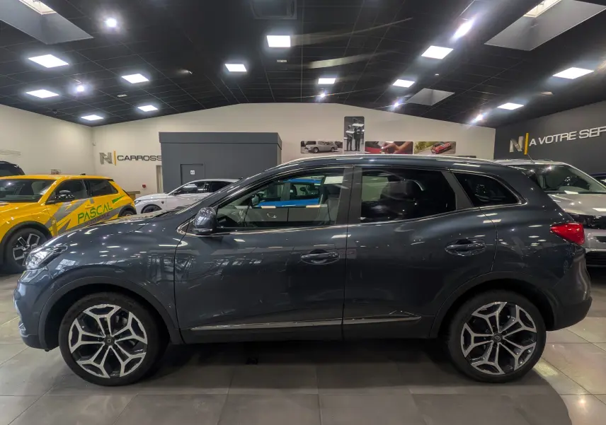 Renault Kadjar TCe 140 Intens gris titanium vu de profil côté gauche dans un showroom lumineux.