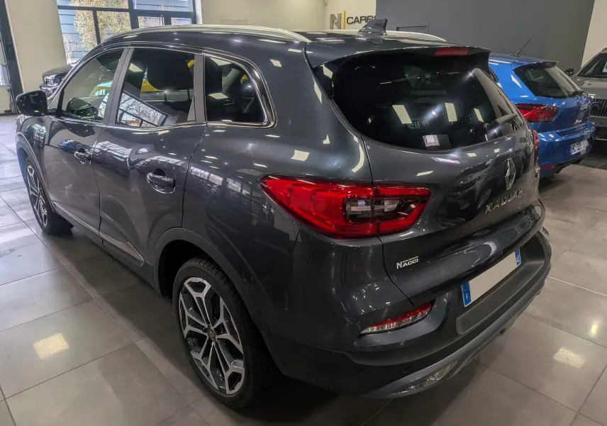 Vue 3/4 arrière droite d’un Renault Kadjar gris titanium en showroom, avec feux arrière LED et jantes alliage distinctives.