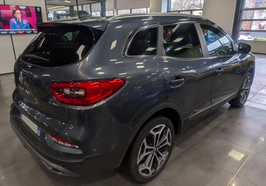 Vue 3/4 arrière droite du Renault Kadjar TCe 140 Gris Titanium, avec jantes alliage et vitres teintées en showroom.