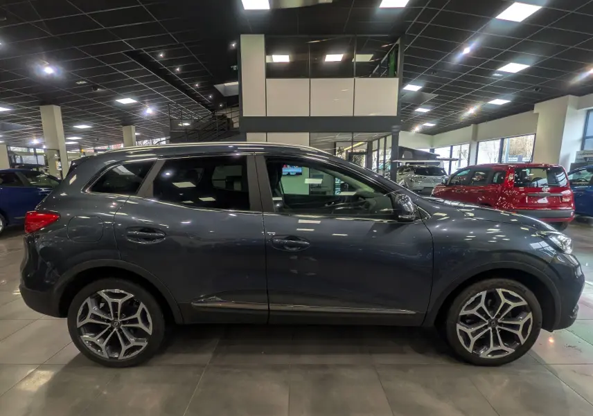 Profil côté gauche d’un Renault Kadjar gris titanium 2019 en showroom, avec jantes alliage et vitres teintées.