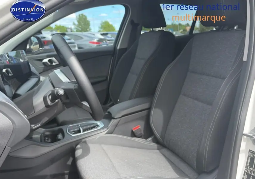 Vue intérieure côté conducteur de la BMW Série 1 blanche, sièges sport gris avec accoudoir central et volant cuir.