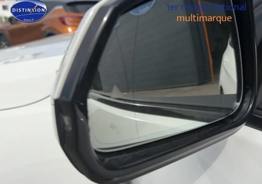 Rétroviseur extérieur côté gauche d'une BMW Série 1 blanche pure, avec reflet du véhicule et arrière-plan flou.