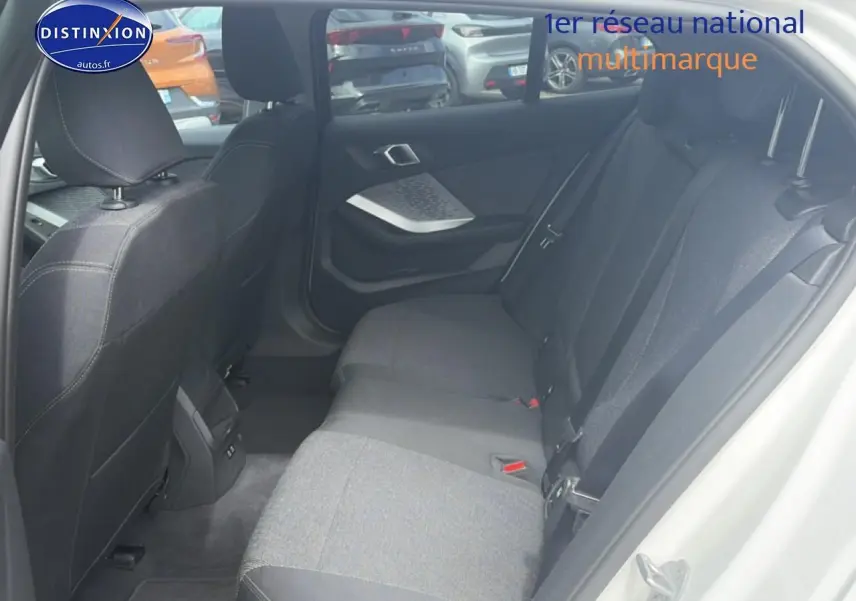 Vue intérieure arrière côté droit de la BMW Série 1 blanche, montrant la banquette tissu et les portes ouvertes.