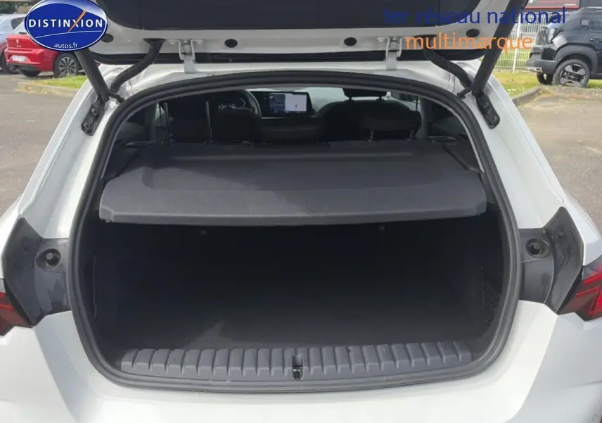 Vue arrière ouverte du coffre d'une BMW Série 1 blanche, montrant l'espace de chargement et la plage arrière.