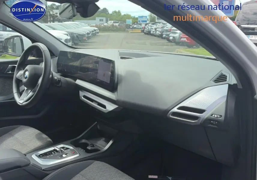 Vue intérieure côté passager de la BMW Série 1 blanche, avec tableau de bord moderne et écran tactile large.