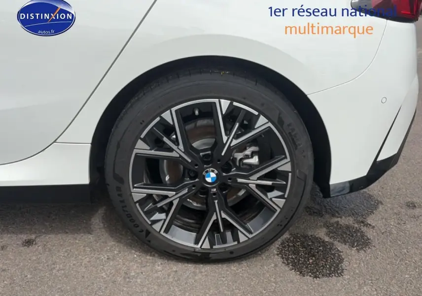 Gros plan sur la roue arrière droite d'une BMW Série 1 blanche avec jante alu noire et grise design M Sport.