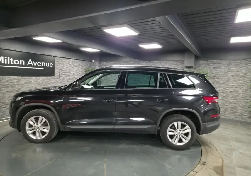 Vue de profil côté gauche d'un SUV Skoda Kodiaq noir métallisé 7 places dans un showroom intérieur.