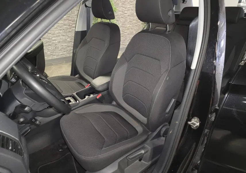 Vue intérieure côté conducteur du Skoda Kodiaq noir 2023, sièges tissu Ambition avec accoudoir central et volant multifonctions.