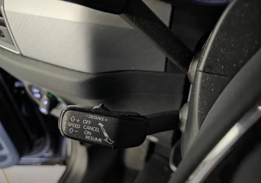 Gros plan sur la commande du régulateur de vitesse adaptatif à gauche du volant dans un intérieur noir du Skoda Kodiaq 2023.
