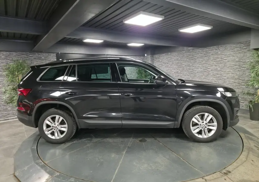 Vue de profil côté gauche d'un SUV Skoda Kodiaq noir métallisé, avec jantes alliage 17 pouces dans un showroom.