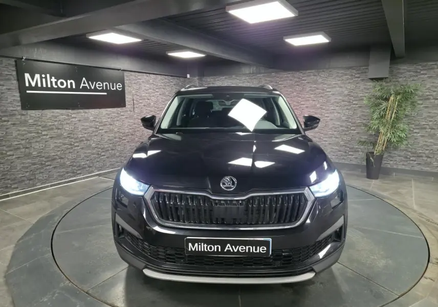 Vue avant d'un Skoda Kodiaq noir 2023 avec phares allumés dans un showroom intérieur.