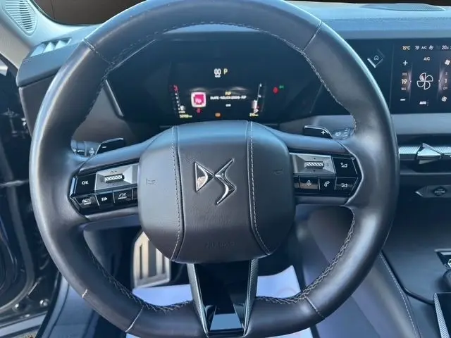 Vue rapprochée du volant cuir noir de la DS4 2022 avec commandes intégrées et tableau de bord numérique en arrière-plan.