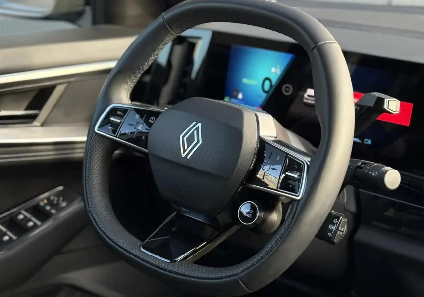 Gros plan sur le volant noir texturé du Renault Austral 2025 avec commandes intégrées et tableau de bord numérique en arrière-plan.