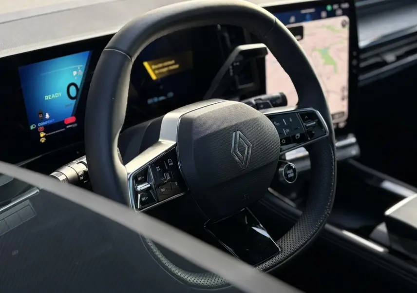 Vue rapprochée du volant noir texturé avec logo Renault, tableau de bord numérique et écran tactile du Renault Austral 2025.