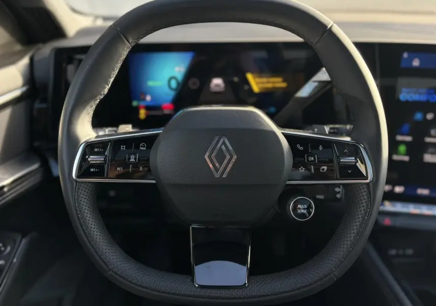 Vue rapprochée du volant noir perforé du Renault Austral 2025 avec commandes intégrées et tableau de bord numérique en arrière-plan.