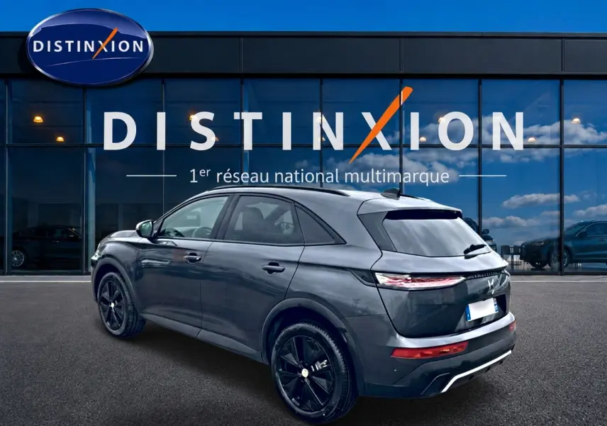 Vue 3/4 arrière droite d'un DS7 gris titane avec jantes noires, garé devant une vitrine Distinxion.