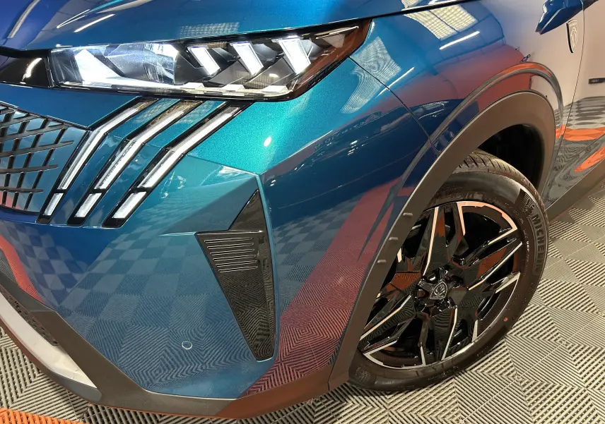 Gros plan sur l'avant droit bleu obsession du Peugeot 3008 III Hybrid 145 avec phares LED et jante noire brillante.