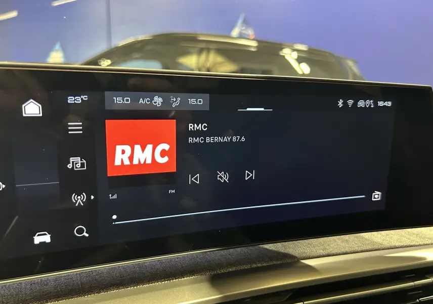 Écran tactile central du Peugeot 3008 III Hybrid 145 GT affichant la radio RMC, intérieur sombre avec reflet extérieur.