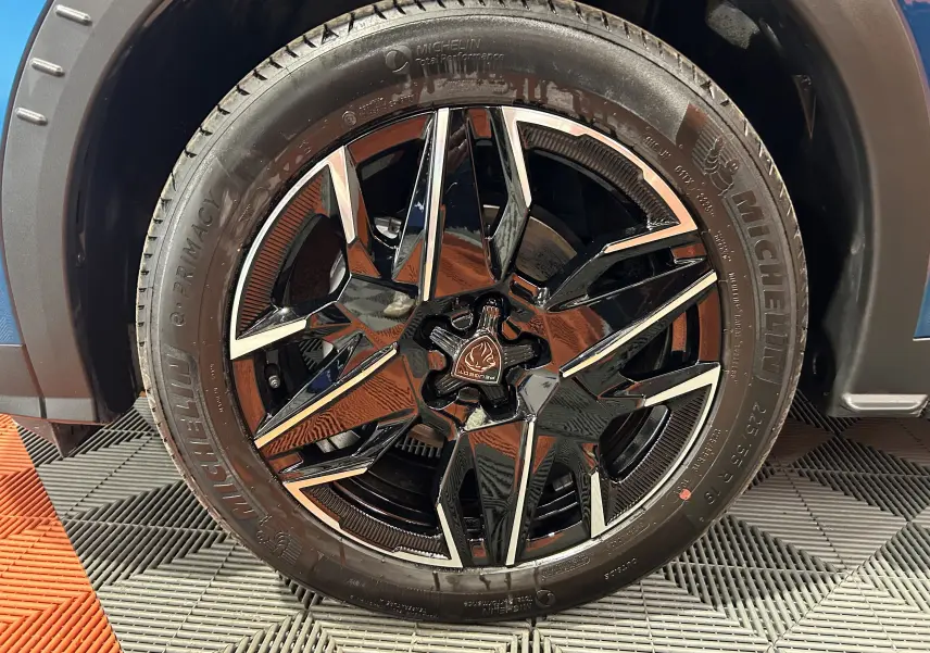Gros plan sur la roue avant gauche du Peugeot 3008 bleu Obsession, mettant en valeur la jante noire brillante au design géométrique.