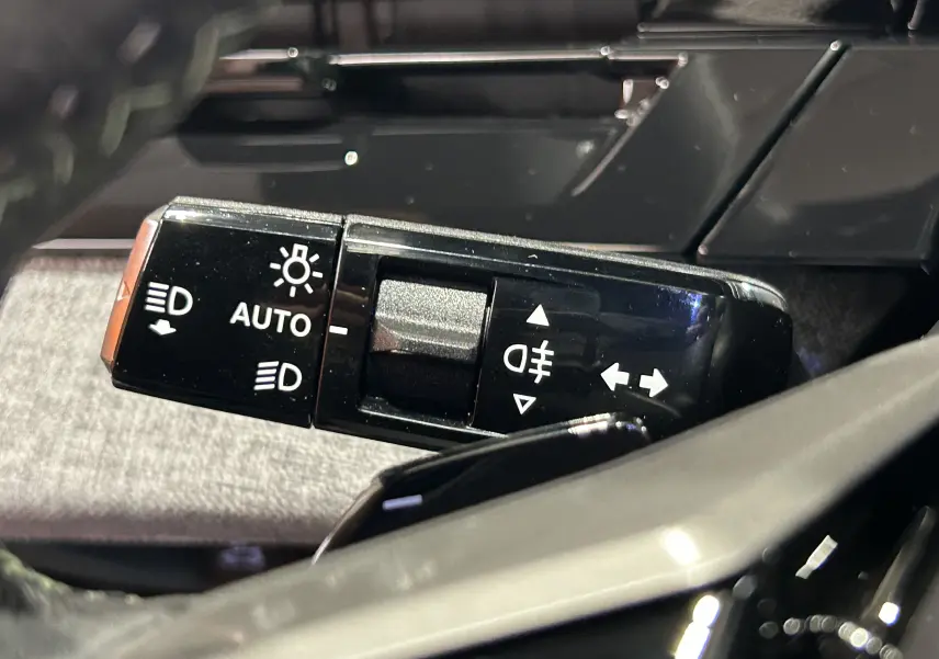 Gros plan sur la commande des feux et clignotants du Peugeot 3008 III Hybrid 145 e-DCS6 GT, intérieur noir et gris.