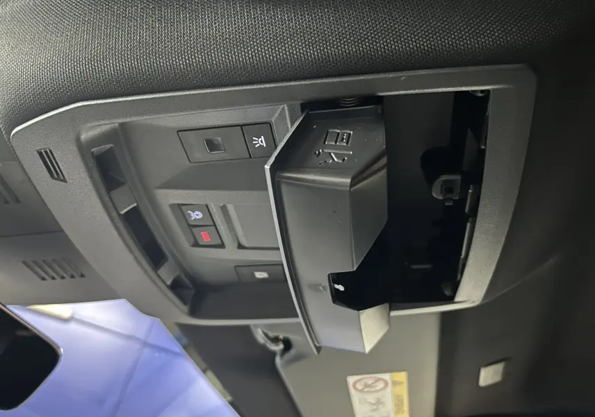 Gros plan sur la console de toit intérieure du Peugeot 3008 III Hybrid 145, montrant les boutons de commande et un compartiment ouvert.