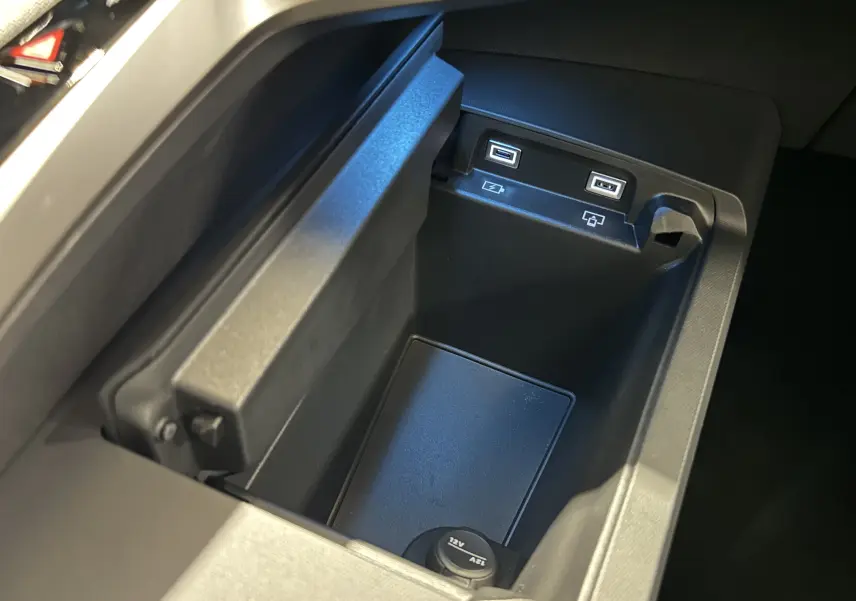 Gros plan sur la console centrale du Peugeot 3008 III Hybrid avec ports USB et prise 12V, intérieur noir.