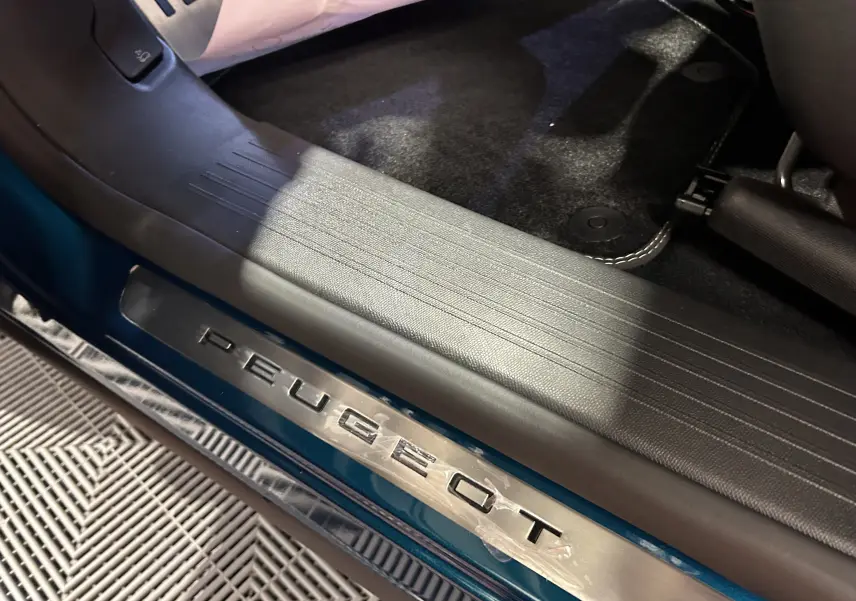 Gros plan sur la plaque de seuil de porte Peugeot, avec la carrosserie bleu obsession visible en partie sous la lumière.